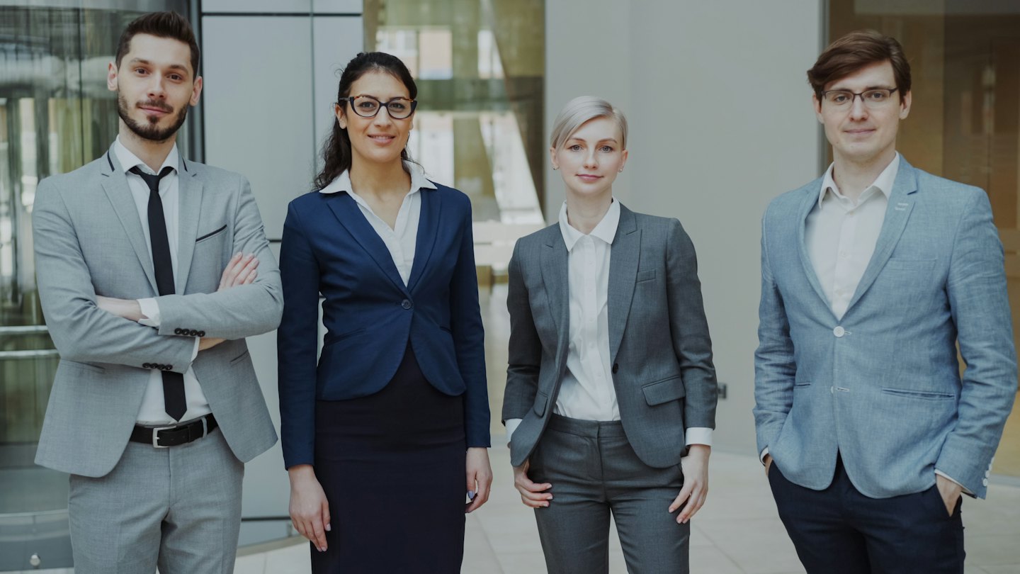 Vier diverse zakelijke professionals in pak staan samen in een kantoor.